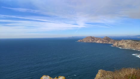 Immensity-of-the-sea-with-the-rocky-mountain-islands-with-residual-clouds-to-the-horizon-on-a-sunny-summer-day,-panoramic-shot-turning-right,-Cíes-Islands,-Pontevedra,-Galicia,-Spain