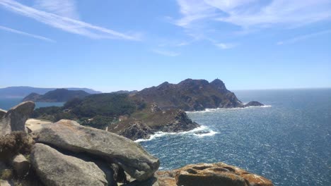 Mountainous-island-with-cliffs-and-beaches-and-camping-in-the-background,-sunny-day,-blocked-elevated-panoramic-shot,-Cíes-Islands,-Pontevedra,-Galicia,-Spain