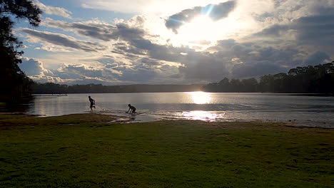 Children-playing-and-running-at-the-edge-of-a-lake-at-sunset,-dawn