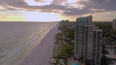 Drone-view-flying-down-the-white-sand-beach-of-San-Destin-FL-during-golden-hour-with-lots-of-clouds-in-the-sky