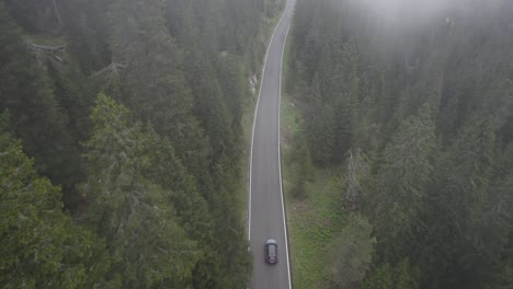 Drone-shot-of-a-car-driving-on-an-empty-road-in-the-middle-of-the-forest-in-Passo-Giao,-Italy