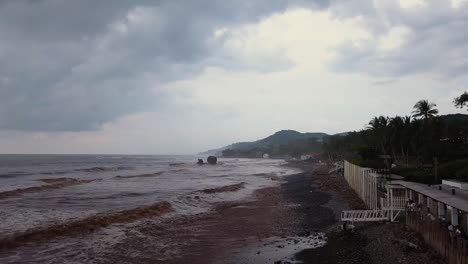 The-boardwalk-at-the-popular-surf-spot,-El-Tunco-beach-in-El-Salvador,-during-an-overcast-and-cloudy-day---Aerial-footage-Dolly-in