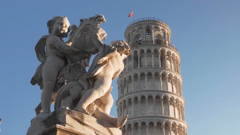 Close-up-of-the-Leaning-tower-of-pisa-with-clear-blue-sky-in-the-morning-during-golden-hour-with-statue-in-the-foreground-filmed-with-a-gimbal-and-a-dolly-movement-in-tuscany,-italy