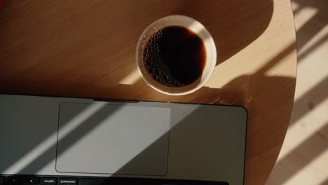 Top-Down-Shot-of-hot-coffee-in-a-mug-next-to-laptop-in-home-office