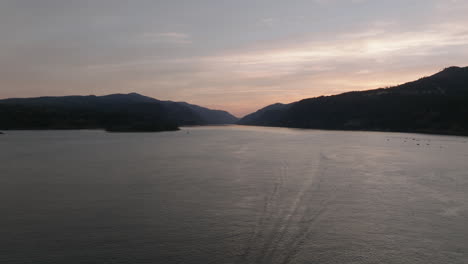 Drone-aerial-of-Columbia-Gorge-at-sunset-as-a-a-motor-boat-speeds-under-the-camera