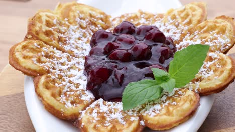 Close-Up-of-a-plate-with-waffle,-powdered-sugar-and-hot-cherry-sauce-on-top