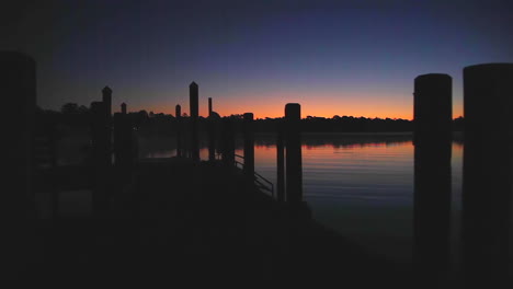 Tracking-shot-of-a-river-dock-in-silhouette-at-sunrise