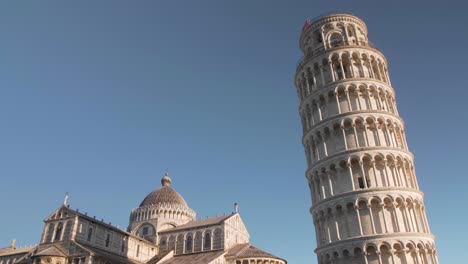 Still-shot-of-leaning-tower-of-pisa-in-tuscany-with-three-birds-flying-to-the-left,-golden-hour,-morning-clear-blue-sky