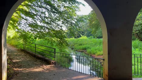 Dolly-shot-moving,-walking,-forward-through-an-archway-to-reveal-a-creek-and-beautiful-scenery