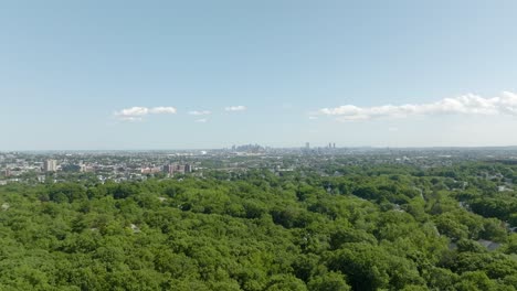 Aerial-flying-above-woods,-tracking-Boston-skyline-in-distance