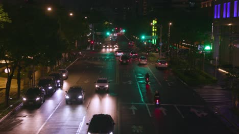 Tráfico-De-La-Calle-Por-La-Noche-En-Taipei-Con-Automóviles-Y-Scooters-Con-Los-Faros-Encendidos:-Plano-General
