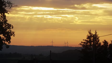 Golden-sunrise-sunset-at-rural-area-with-wind-power-plant-visible-on-the-hills