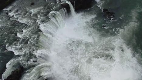 Drone-hovering-over-a-large-circulair-waterfall-with-the-camera-tilting-down-slowly-in-Iceland-in-4k