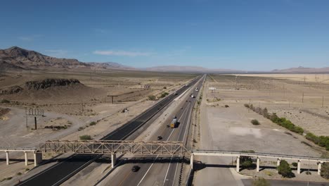 Aerial-view-of-Highway-in-Desert,-Cars-Trucks-Semis-Driving,-Interstate-15-Primm-Nevada,-Mountains-and-Blue-Skies