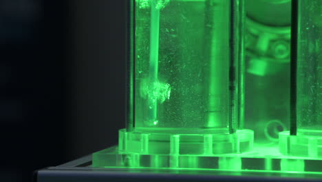 Hydrogen-gas-bubbles-in-tubes-with-water-in-a-electrolyzer-demonstrator,-green-light,-slow-motion