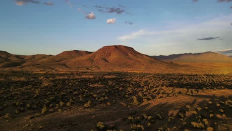 Aerial-View,-Drone-Flying-Towards-a-Butte-in-the-Desert-at-Sunset,-Brush-and-plants-in-Foreground,-Light-Blue-Skies,-Golden-Hour-in-Arizona