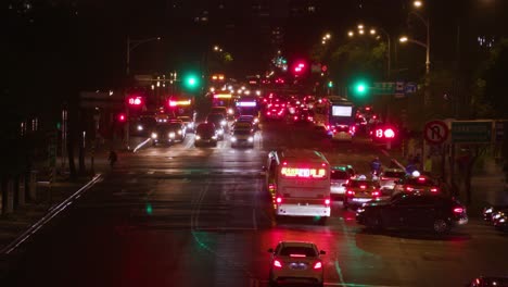 Busy-street-traffic-at-night-in-Taipei-with-cars-and-buses-with-headlights-on-while-traffic-lights-turn-red-to-green-–-wide-shot