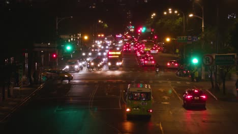 Busy-street-traffic-at-night-in-Taipei-with-traffic-lights-turning-red-to-green-while-a-bus-crosses-the-avenue-from-left-to-right-–-wide-shot