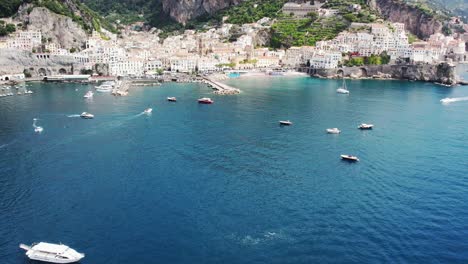 Drone-flying-over-sea-towards-a-coastal-village-starting-with-the-camera-downwards-tilting-upwards-on-the-Amalfi-coast-in-Italy-4k