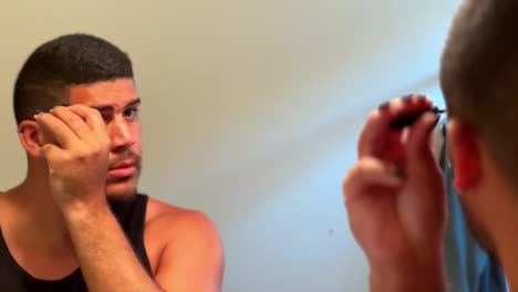 Gay-mixed-race-man-looking-into-mirror-adding-eyebrow-makeup-in-bathroom,-close-up-LGBTQ