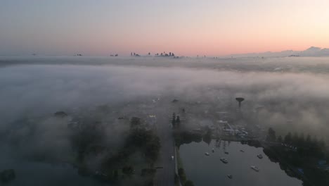 Foggy-Sydney-skyline-at-sunrise,-beautiful-reverse-flying-over-Princess-Highway-with-traffic-in-the-morning
