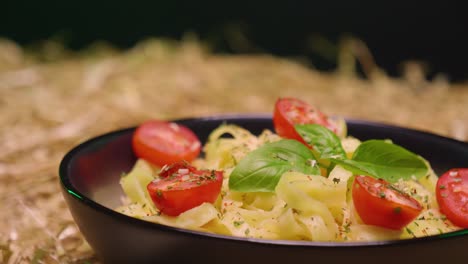 Pullback-Cerca-De-Un-Plato-Con-Deliciosa-Pasta,-Tomates-Y-Albahaca-Y-Crema-Agria-En-El-Lado-Colocado-Sobre-Paja