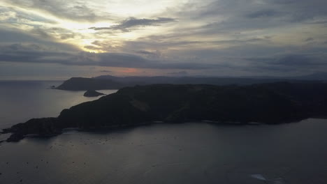 Cloudy-dusk-sunset-aerial-rises-over-calm-bays-of-south-Lombok,-IDN