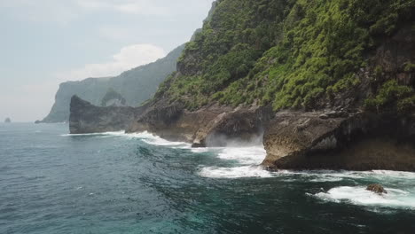 Ocean-waves-break-against-base-of-steep-tropical-jungle-cliffs-in-Bali