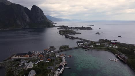 Reine,-Norway---Aerial-flying-over-fisher's-village-houses-located-on-Lofoten-isles-connected-with-E10-highway-and-bridges,-view-of-ocean-bay-with-rocky-mountains