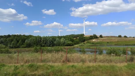 Shot-of-driving-past-wind-turbines-creating-renewable-energy-in-a-vehicle-on-the-road,-4K