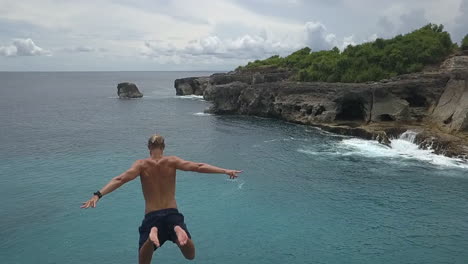 Following-aerial-as-young-man-leaps-off-cliff-into-Bali-sea-far-below