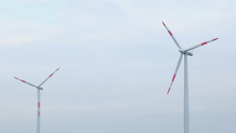Shot-of-a-two-wind-turbines-creating-renewable-energy,-one-spins-very-fast,-other-one-slowly,-4K