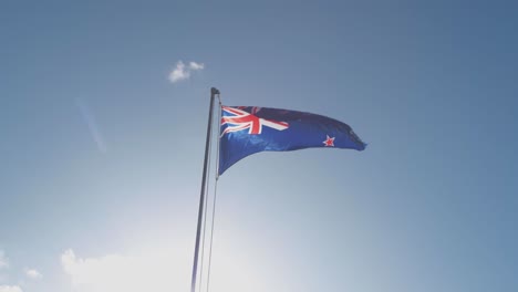 Una-Bandera-De-Nueva-Zelanda-Ondea-En-Un-Poste-Con-Cielo-Azul-Y-Bengalas-Solares