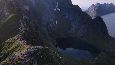 Aerial-flying-along-steep-cliffy-Reinebringen-mountain-ridge-with-hiking-trail-revealing-fjords-and-Lofoten-islands-rocky-summits