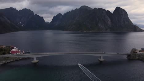 Aerial-flying-over-a-bridge-connecting-Kvalvika-and-Sakrisoy-islands-and-view-of-rocky-mountains-of-Lofoten,-Reine,-Norway