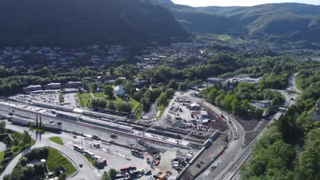 Arna-train-station-and-road-E16-with-dense-populated-lush-green-mountain-landscape-background---Sunny-summer-day-aerial-view-outside-Bergen-Norway