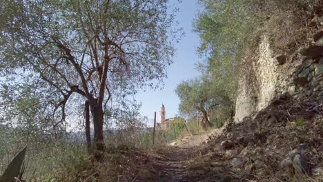 SLOWMOTION:-Beautiful-path-in-Prelà-Castello-Italy-surrounded-by-olive-trees-and-centered-view-of-an-old-italian-mountain-church-on-a-sunny-summerday
