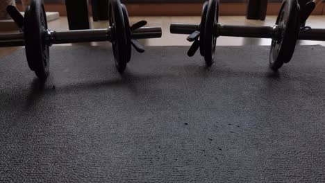 A-dolly-shot-moving-backwards-focused-in-two-dumbbells-standing-on-a-black-mat