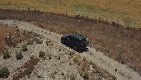 A-drone-shot-following-a-green-car-going-on-a-trail-between-dry-plants
