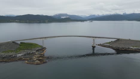 Flying-over-Atlantic-Ocean-Road-in-Norway-with-cars-passing-the-lonely-bridge-on-an-overcast-and-cloudy-day-in-Summer