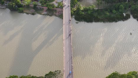 Topdown-view-Follow-vehicles-driving-along-bridge-road-over-Muddy-river,-Bangladesh