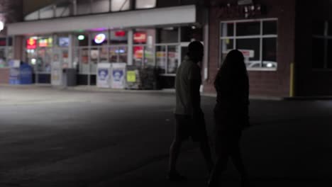 Panning-Shot-Of-A-Young-Couple-Walking-Past-A-Gas-Station-At-Night