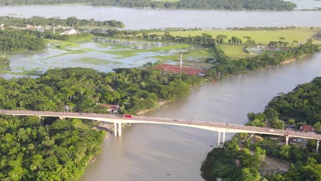 Drone-flying-towards-Congrete-Brigde-with-traffic,-connecting-two-forested-areas,-Bangladesh