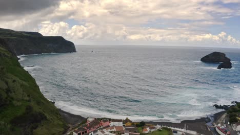 Waves-washing-black-sand-beach-of-coastal-bay,-Azores,-zooming-aerial