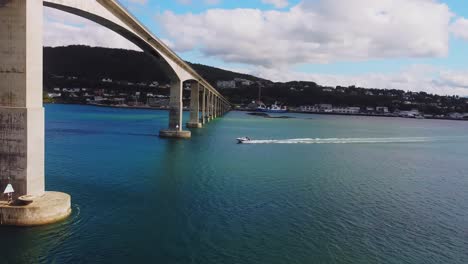 Luftaufnahme-Der-Inselbrücke-Senja,-Norwegen,-Aufschlussreiche-Drohnenaufnahme-Eines-Bootes,-Das-An-Einem-Sonnigen-Sommertag-Unter-Einer-Modernen-Kreuzung-Segelt