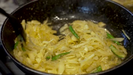 A-close-up-shot-of-fresh-onions-and-chillies-sautéing-on-a-hot-oily-frying-pan-as-a-chef-carefully-stirs-the-vegetables-cooking-on-a-kitchen-stove