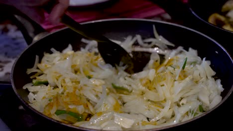 A-close-up-shot-of-the-hand-of-a-chef-carefully-stirring-freshly-chopped-raw-onions-and-green-chillies-in-a-hot-non-stick-frying-pan-with-a-spatula