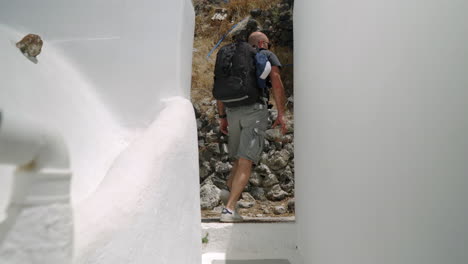 Following-a-man-wearing-a-backpack,-walking-down-a-narrow-street-of-a-Greek-island