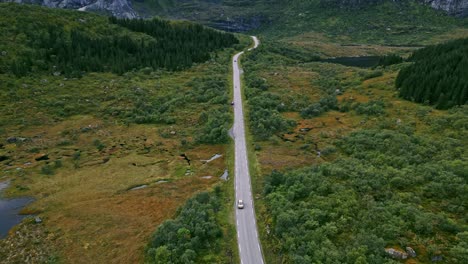 Panning-flying-shot-in-front-of-golden-car-driving-along-the-scenic-road-in-Lofoten-Norway-revealing-a-panoramic-scenery-of-dramatic-mountains-and-lakes