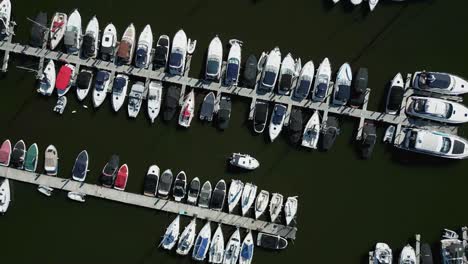 Statischer-Lookdown-Luftdrohnenblick-über-Bootsliegeplätze-Und-Farbenfrohe-Yachten-Am-Jachthafen-Von-Bowness-Am-Lake-Winderemere-Mit-Einem-Kleinen-Boot,-Das-Sich-An-Einem-Sonnigen-Sommermorgen-Durch-Die-Szene-Bewegt